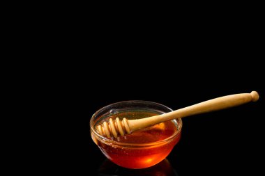 Honey in bowl with wooden stick isolated on black background.