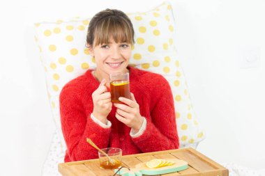 Young woman in bed with a slice of lemon, herbal tea and honey.