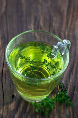 Thyme (thymus vulgaris) herbal tea viewed from above in a glass cup on the background of old board.