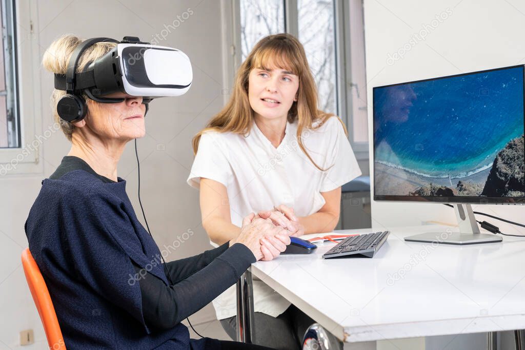 Elderly woman, during a therapy session with a virtual reality headset under the supervision of a therapist.