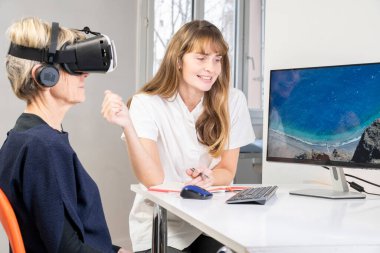 Elderly woman, during a therapy session with a virtual reality headset under the supervision of a therapist.