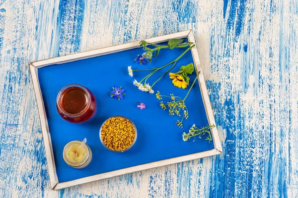 Honey, pollen and royal jelly with medicinal plants deposited on a tray in top view.