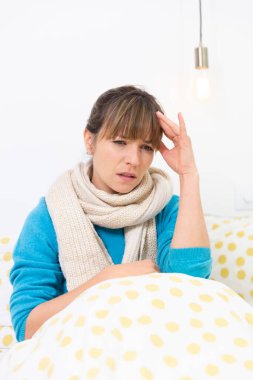 A young woman wrapped up in bed suffering from a flu-like condition with a migraine.