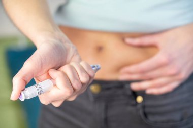 Close-up of a woman's hands and stomach giving herself an insulin injection.
