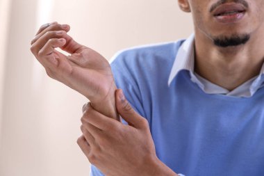 Close up of man suffering from pain in his wrist on pink background.