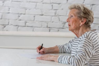 Senior woman writing on a white sheet.