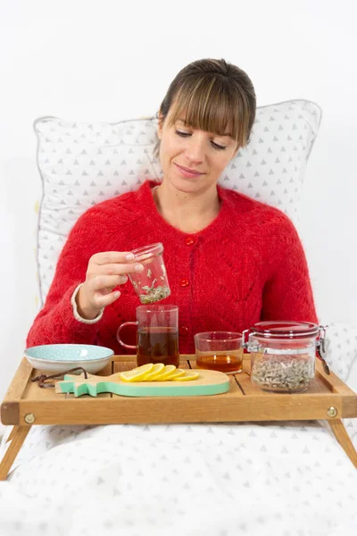 Young woman in bed with honey herbal tea and a sliced lemon.