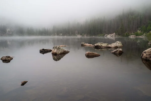 Felsen spiegeln sich in einem nebligen See — Stockfoto