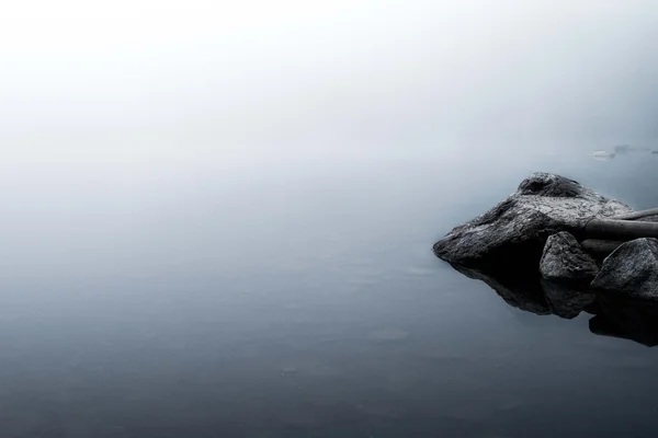 Reflections of rocks in a foggy lake
