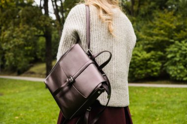 Örgü ceketli genç bir kızın arka görüntüsü. Bir omuzda şık deri bir sırt çantası. Sonbahar parkı. Sonbahar modası..