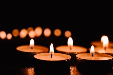 Karanlıkta yanan çay mumlarına yakın çekim. Mum ışığı alevinin yansıması.