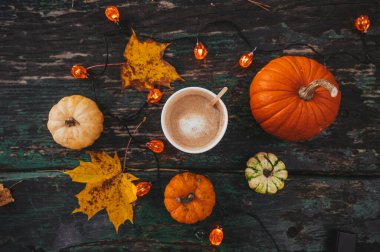 Sonbahar yatağı. Karton bardakta kahve. Balkabağı. Akçaağaç yaprakları. Çelenk ışıkları. Eski ahşap masa.