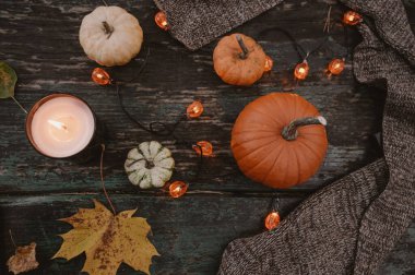 Balkabağı, çelenk, mum, dökülen yapraklar ve eski ahşap masaya örülmüş yün eşarp. Sonbahar bileşimi.