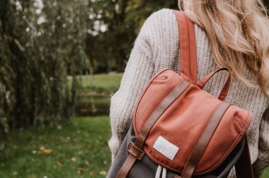 Örgü ceketli genç bir kızın arka görüntüsü. Havalı bir sırt çantası. Sonbahar modası. Şehir parkında yürürken.