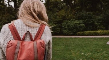 Örgü ceketli genç bir kızın arka görüntüsü. Havalı bir sırt çantası. Sonbahar modası. Şehir parkında yürürken.