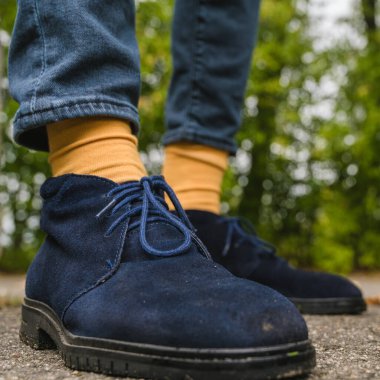 Mavi süet ayakkabılı ve sarı çoraplı bacaklar. Düşmüş yapraklı asfalt. Erkekler için sonbahar modası.