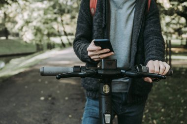Elinde telefon olan ve elektronik scooter kiralamak için mobil uygulama kullanan bir adam. Yakın plan. Modern eko kentsel ulaşım.