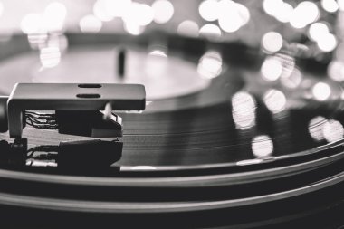 Vinil bir pikabın yakın plan çekimi. Arka planda Bokeh 'in ışıklı çelenkleri var. Siyah ve beyaz.