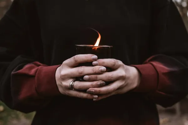 Close-up of burning black candle in woman`s hands. Black and red sweater.