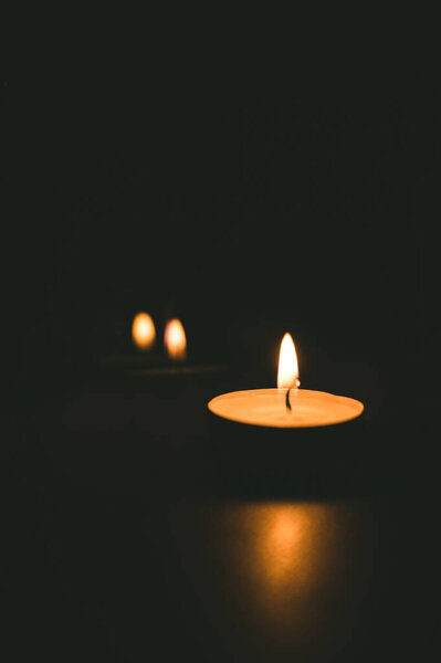 Close-up of burning tea candle in the dark. Reflection of candlelight flame.