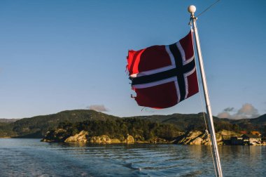 Fiyort 'un arka planında Norveç bayrağı sallıyor. Güneşli bir günde Lusefjord 'da dolaşmak. Lüks turizm.