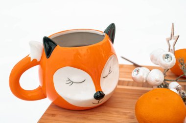 Winter composition. Tangerines, mug in shape of fox and a decorative twig on a wooden board on snow. Top view.