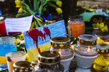 Riga, Letonya 'daki Ukrayna Büyükelçiliği' ndeki savaşı protesto etmek. Mumlar ve çiçekler. Kırmızı lekeli Ukrayna bayrağı