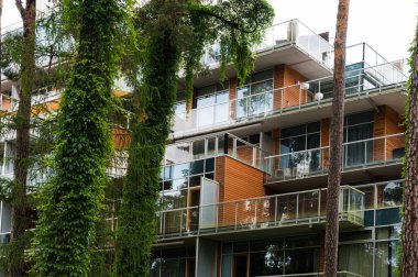 Part of facade of luxury building near trees. Modern residential house. Glass balcony.