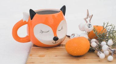 Winter composition. Tangerines, mug in shape of fox and a decorative twig on a wooden board on snow. Top view.