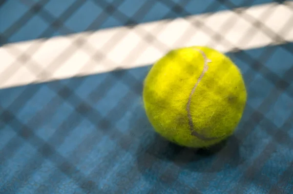 Close-up of yellow tenis ball  on blue hard tenis court. Blurred racket on foreground.