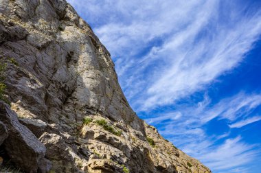 Bottom view of huge rock. Clouds in blue sea. Mountain.