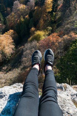 Genç aktif bir kız kayanın kenarında oturuyor, Kafkasya dağlarına bak..