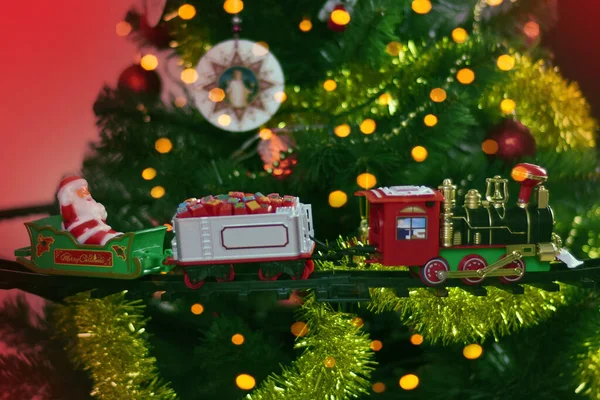 Noel ve yeni yıl kutlaması konsepti, geçmiş. Oyuncak buhar lokomotifi Bokeh Işıkları çelenklerinin arka planında süslü bir Noel ağacında. 