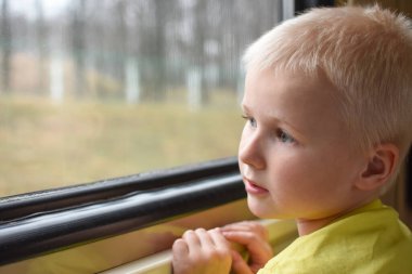 Çocuk trenle seyahat eder ve arabanın camından dışarı bakar.