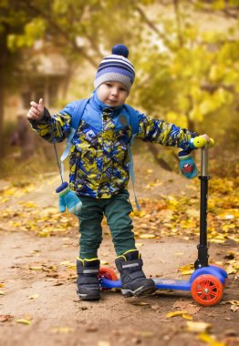 Yakışıklı çocuk sonbahar parkında scooterıyla duruyor.