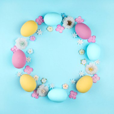 Mavi arkaplanda pembe, mavi ve sarı Paskalya yumurtaları ve çiçekler var.