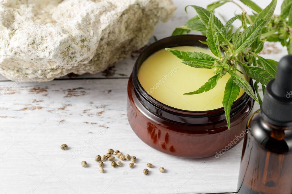 Hemp salve balm and relaxing CBD serum oil as a complex in the homeopathy  treatment of the musculoskeletal or calming nervous system or psoriasis. Composition with female cannabis plant and new seeds on wooden background with copy space
