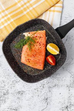 Dilimlenmiş taze somon balığı dereotlu ve maydanozlu taş ızgara tavada ve beyaz siyah masa arkasında mutfak havlusu. Çiğ somon fileto bifteği pişirmek için sağlıklı bir yemek.