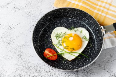  Yeşil soğan ve dereotla tatlandırılmış yağsız kızartma tavasında kızartılmış kalp şeklinde bir yumurta. Sağlıklı kahvaltı konsepti. Tabakta havlu ve taş masa..