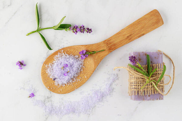 Lavender soap, violet salt on wooden spoon and  fresh flowers on white marble background. Bath body care or spa wellness concept.  Floral card with copy space