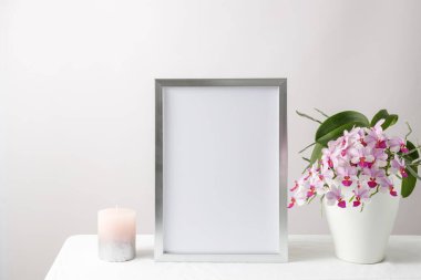 Çiçek kartı ya da poster modeli ya da beyaz masa örtüsünün üzerindeki seramik kapta pembe orkide çiçekleri olan gümüş fotoğraf çerçevesi. Ev dekorasyonu