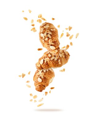 Beyaz arka planda uçuşan fındık kırıntılarıyla birlikte taze pişmiş badem kahvaltı kruvasanları. Üç kruvasan düşüyor. Pasta dükkanı kartı..