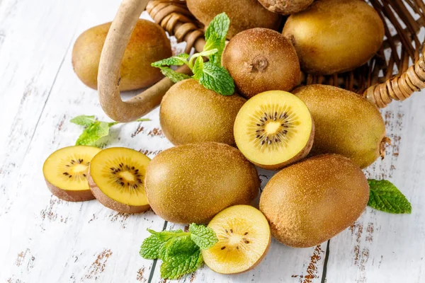 Ripe raw kiwi gold whole and slices falling from basket with mint leaves on rustic wooden table.