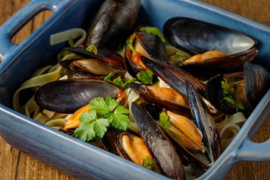 Şili usulü açık midye (Mytilus chilensis L.) ve domatesli makarna ve maydanoz yapraklı tagliatelle ahşap masadaki mavi seramik kasede yakın plan. Sağlıklı deniz ürünleri. Seçici odak