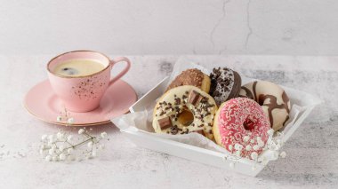 Değişik renklerde pembe, beyaz ve koyu çikolata kaplı çörekler üzerine serpiştirilmiş şekerler ve beyaz ahşap tepside, taş masadaki eski kahve fincanı. Kahve molasında tatlı olarak taze çörek.