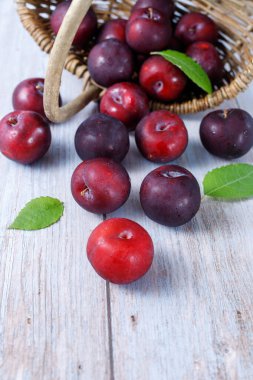 Taze olgun mor erik meyveleri, su damlaları ve sepetten dökülen yapraklar ahşap masaya. Sağlıklı meyve.