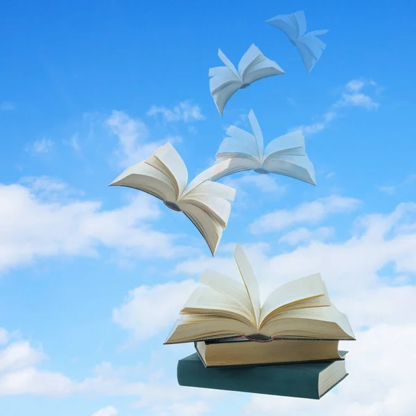 Flying pile of books on blue background with copy space. Open books flying into sky with clouds.