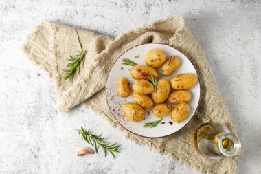 Taze pişmiş, zeytinyağlı, biberiyeli ve keten havlunun üzerine sarımsaklı küçük patatesler. Tabak retro taş masada..