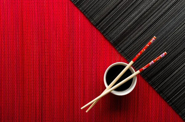 Chopsticks and bowl with soy sauce on bamboo mat — Stock Photo, Image