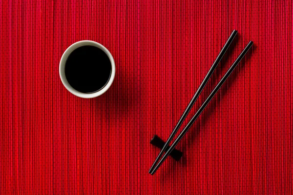 Chopsticks and bowl with soy sauce on bamboo mat — Stock Photo, Image